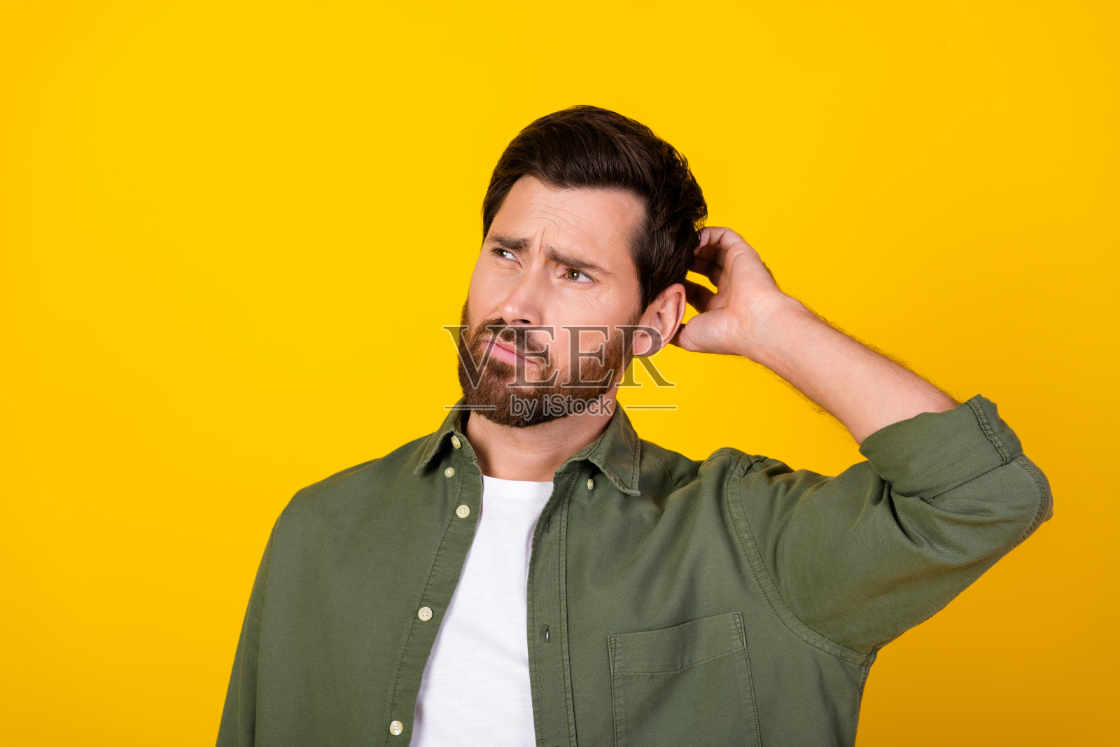 年轻男子的肖像，抓着头，目光空洞，穿着卡其色衬衫，背景为黄色。照片摄影图片