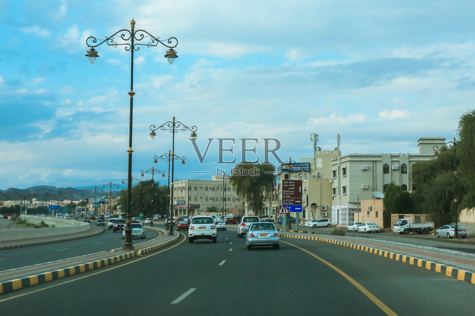 阿曼繁忙的街道,展示华丽的街灯和现代建筑,天空多云。照片摄影图片
