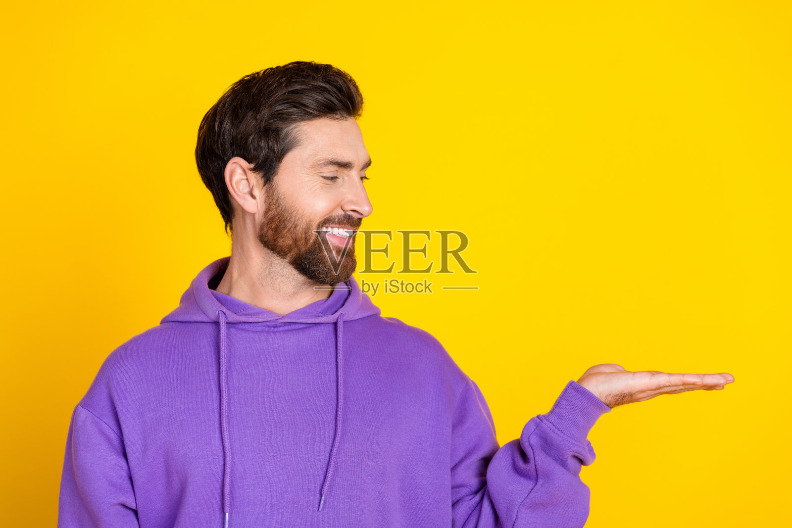 穿着紫色连帽衫的好心情男士，手臂上看着空旷的物体，背景为黄色。照片摄影图片