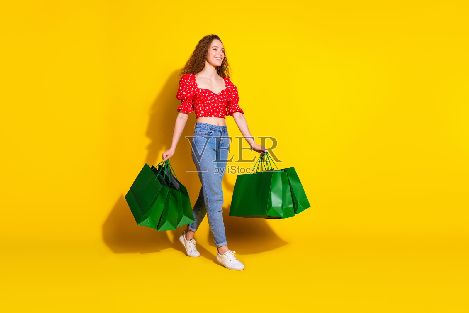 全身照，吸引人的年轻女性手持购物袋，穿着时尚的红色衣服，背景为黄色。照片摄影图片