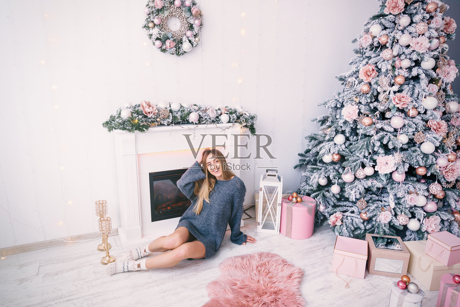 穿着灰色毛衣的女孩坐在壁炉旁，旁边有一棵圣诞树。照片摄影图片