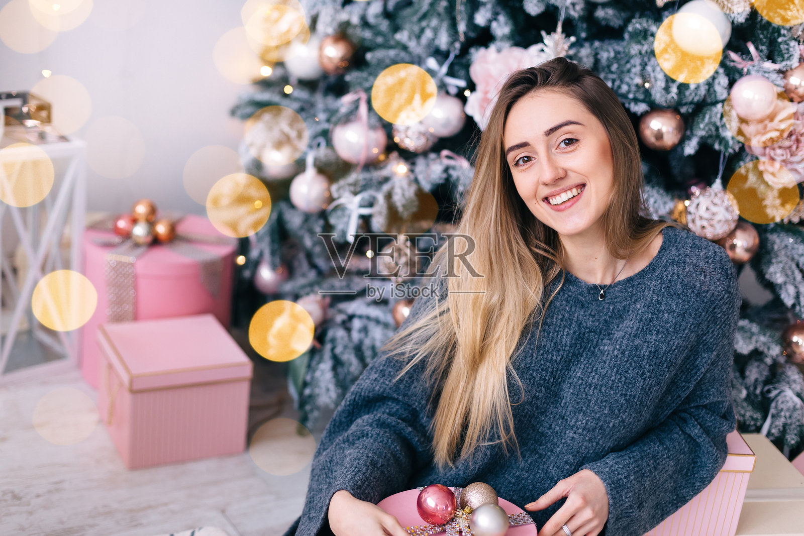 可爱的女孩坐在圣诞树旁，手里拿着一个盒子。照片摄影图片