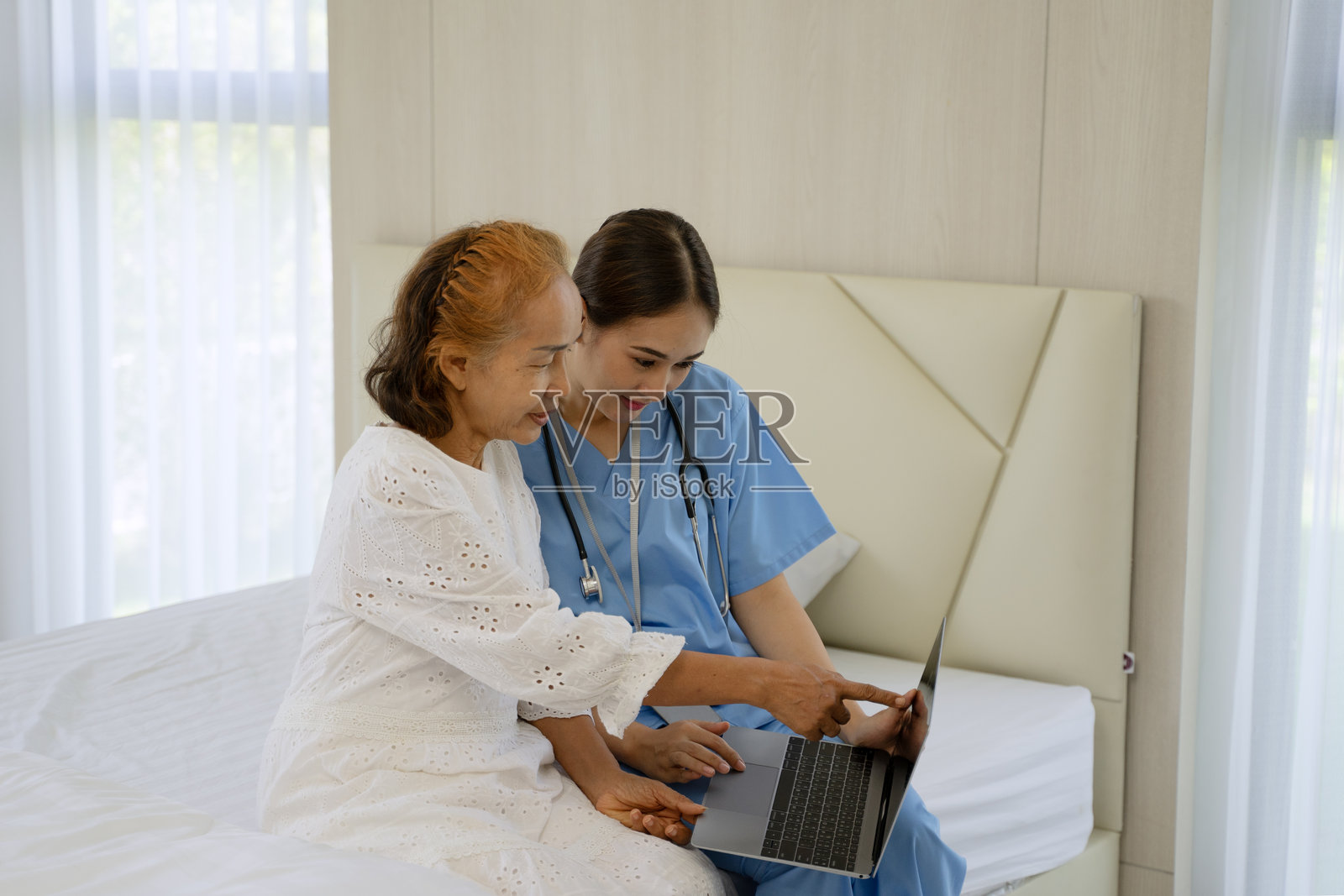 护士在家中照顾一位年长女性，同时使用笔记本电脑。照片摄影图片