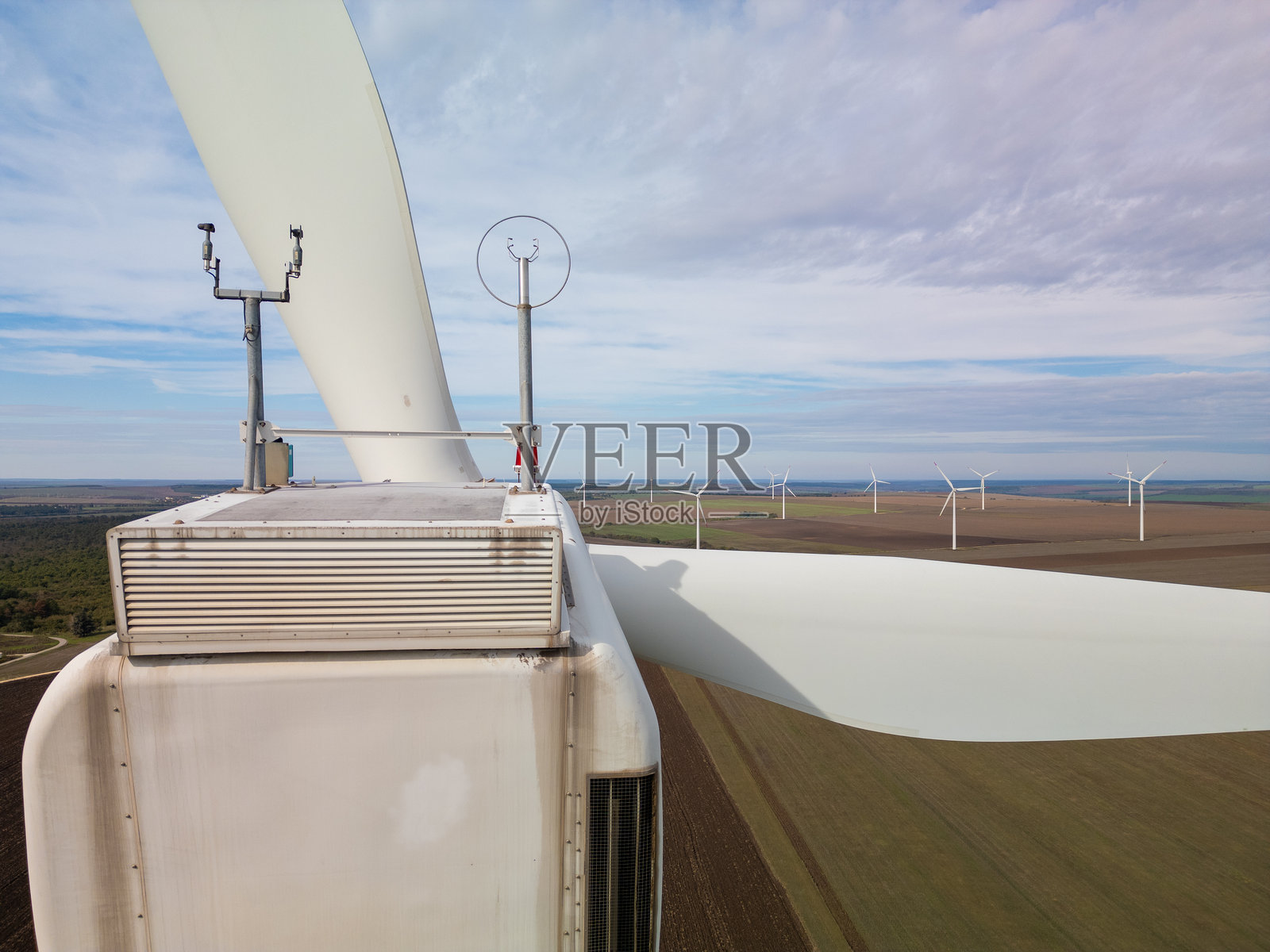 风力涡轮机的鸟瞰近景后视图，详细展示顶部设备，背景中有多个涡轮机俯瞰农田。乡村景观中的可再生能源基础设施。照片摄影图片
