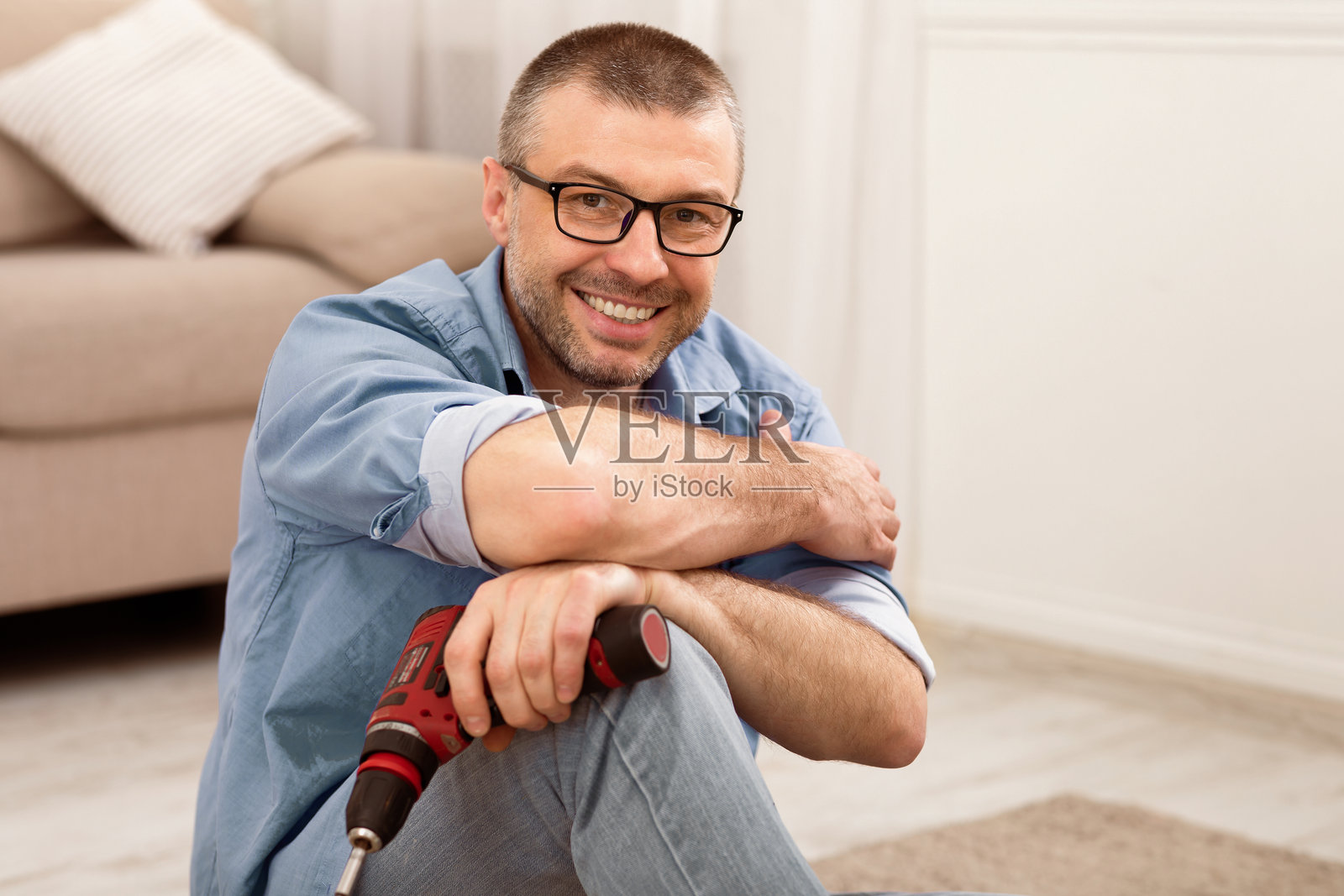 成熟男性在室内坐着，摆姿势使用电钻组装家具照片摄影图片