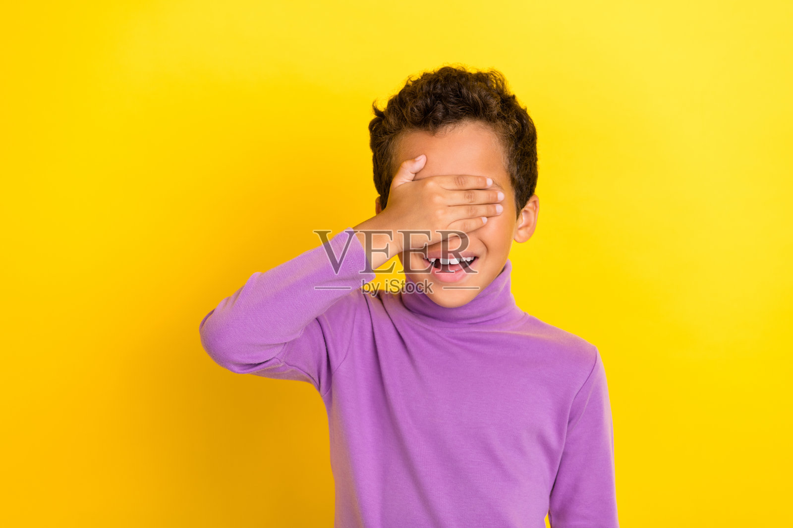 阳光灿烂的学生，露出灿烂的笑容，手臂遮住眼睛，背景为黄色。照片摄影图片