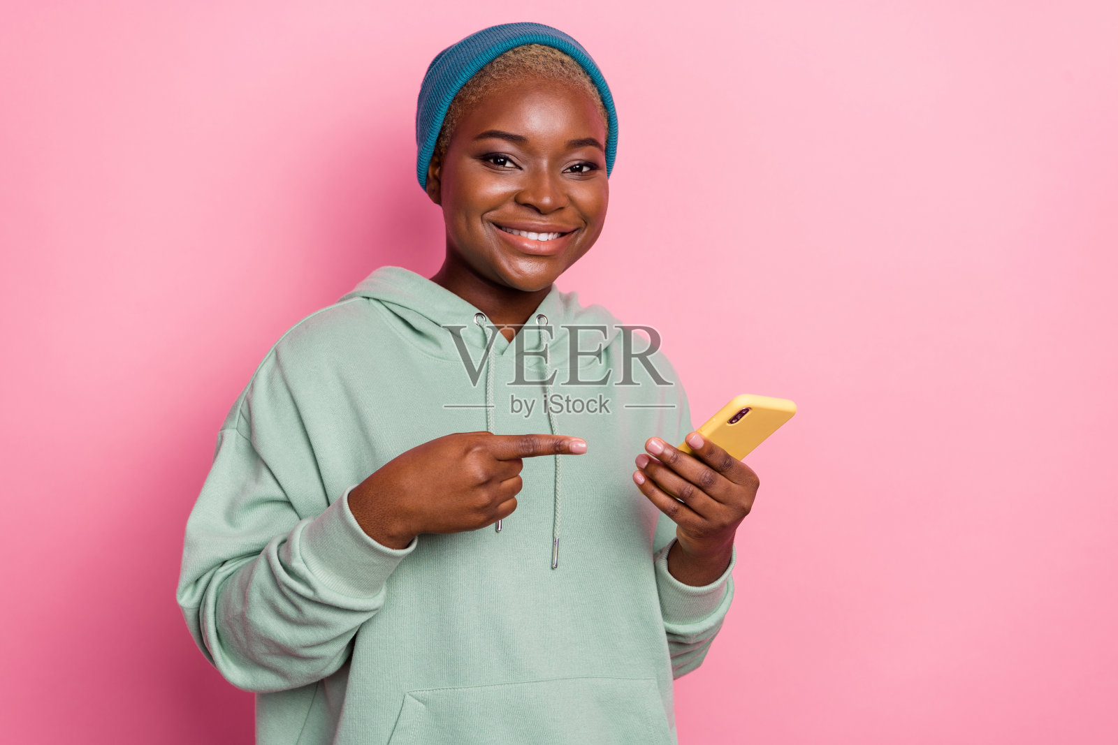 迷人的女性肖像，推荐她的现代手机，背景为粉色。照片摄影图片