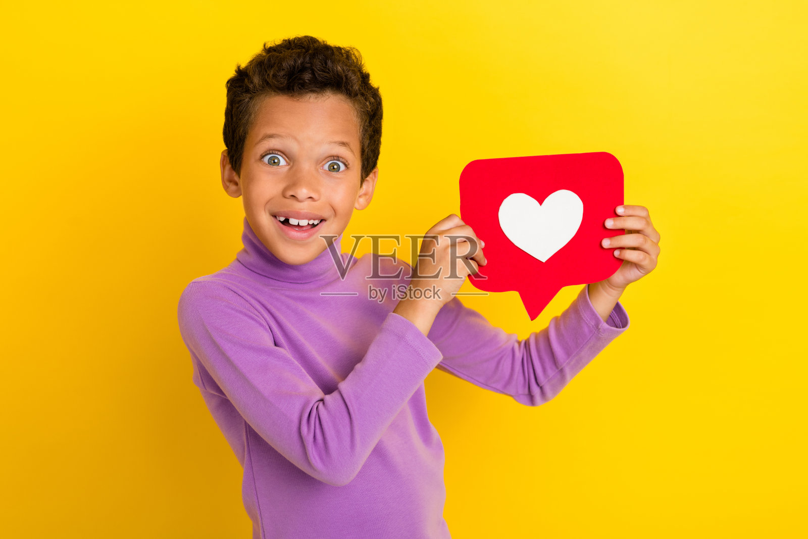 一个搞笑的惊讶男孩，双手举着纸张，露出灿烂的笑容，背景为黄色。照片摄影图片