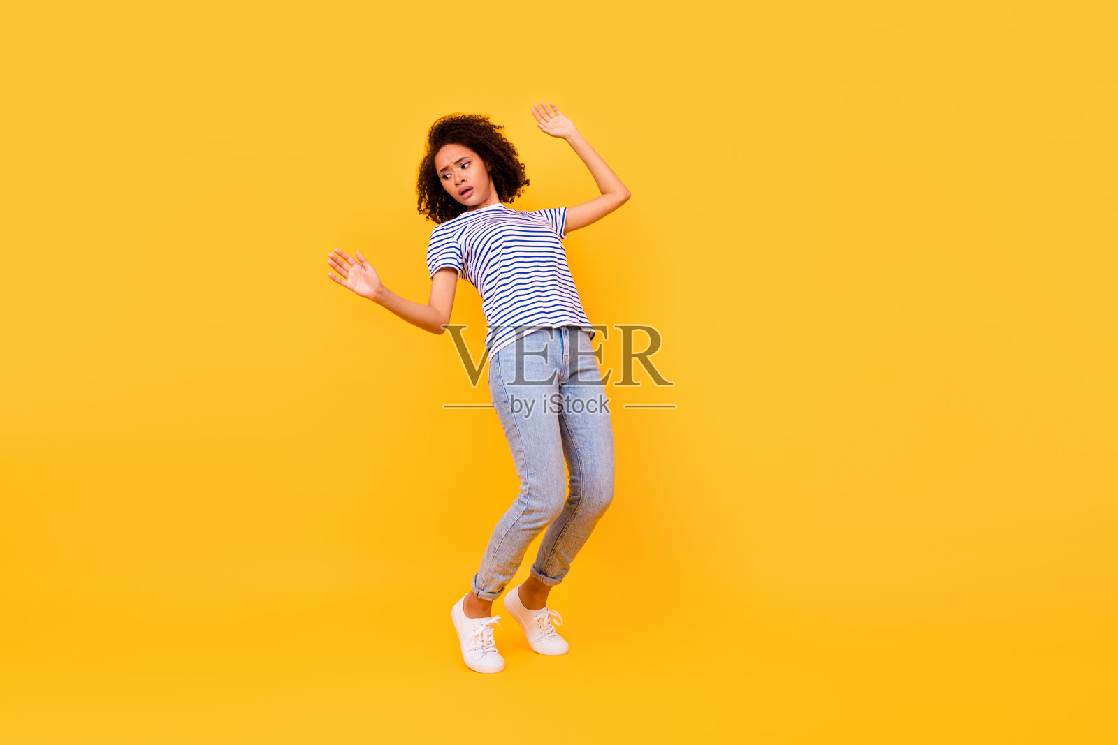 全身照片显示一个紧张的年轻人踮起脚尖，平衡在悬崖边缘的空旷空间，背景为黄色。照片摄影图片