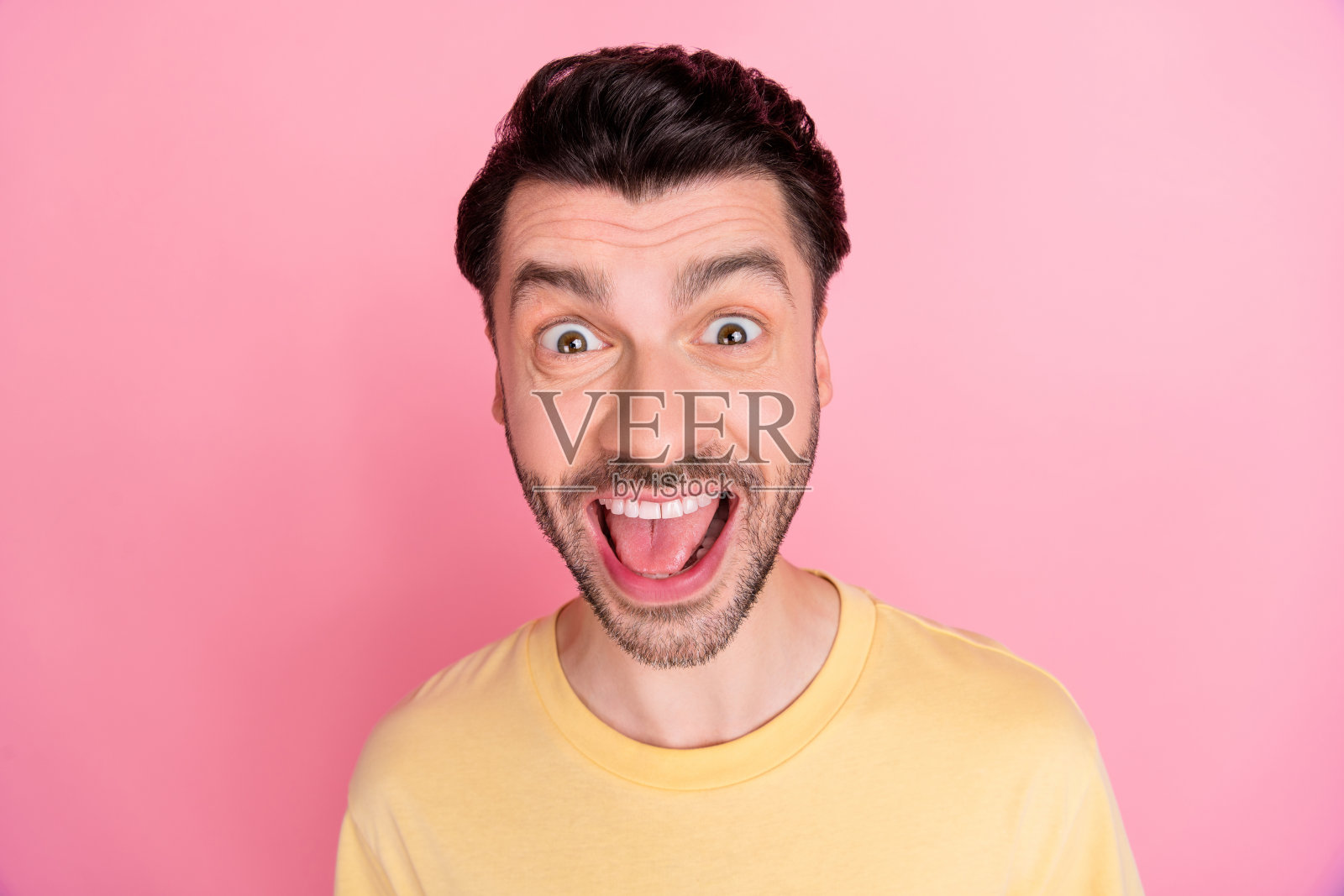 一位充满怀疑、思考且好奇的男子，留着时尚的发型，穿着黄色T恤，目光空洞，独自站在粉色背景前。照片摄影图片