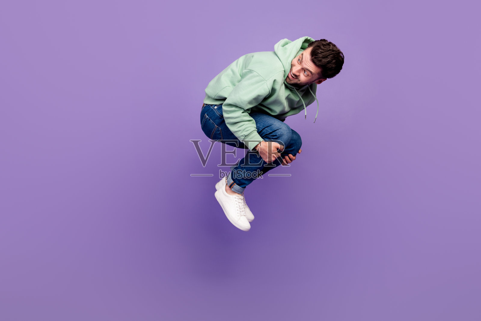 充满活力的活跃人物在紫色背景上跳跃回头，展现全身侧面肖像。照片摄影图片