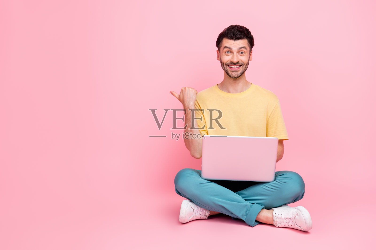 穿着时尚的积极男性坐着，手臂指向空旷的地方，推荐快速的WiFi连接，背景为粉色。照片摄影图片