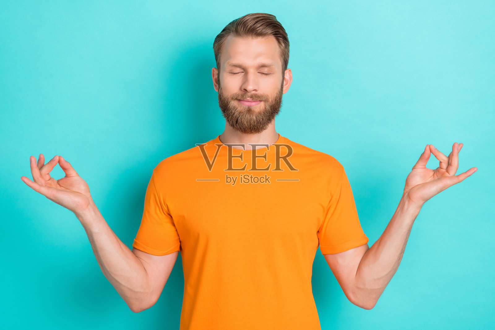 专注冥想的心情愉悦的金发男子，穿着橙色T恤，双眼闭合，背景为青色。照片摄影图片