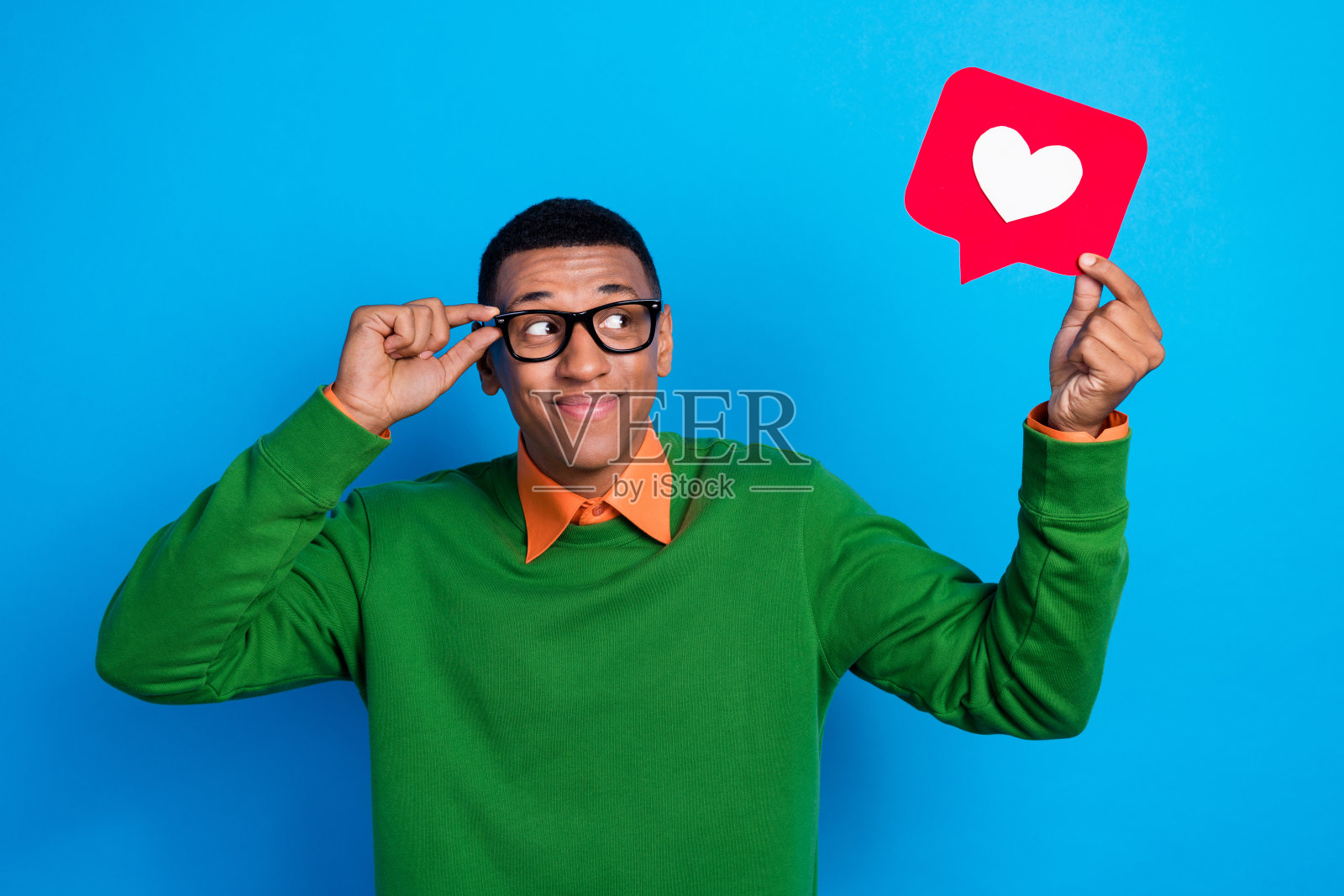 年轻积极的梦想学生男孩，受欢迎的博主，调整眼镜，注视着红色纸张符号，背景为蓝色。照片摄影图片