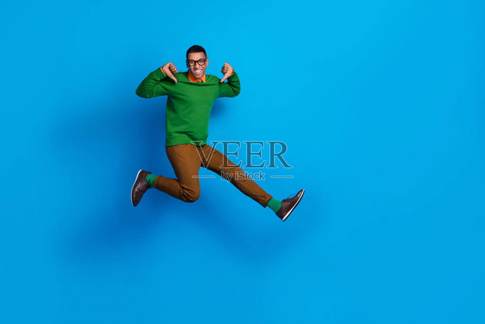 成功的幽默商人在蓝色背景下跳跃，指着自己，展示最佳宣传，展现全身照片。照片摄影图片