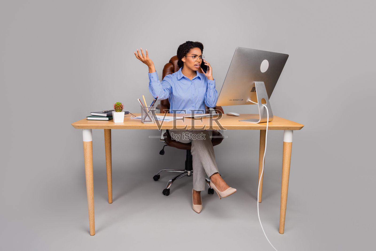 自信的年轻女商人在办公室里一边打电话一边使用电脑，忙碌地处理多项任务。照片摄影图片