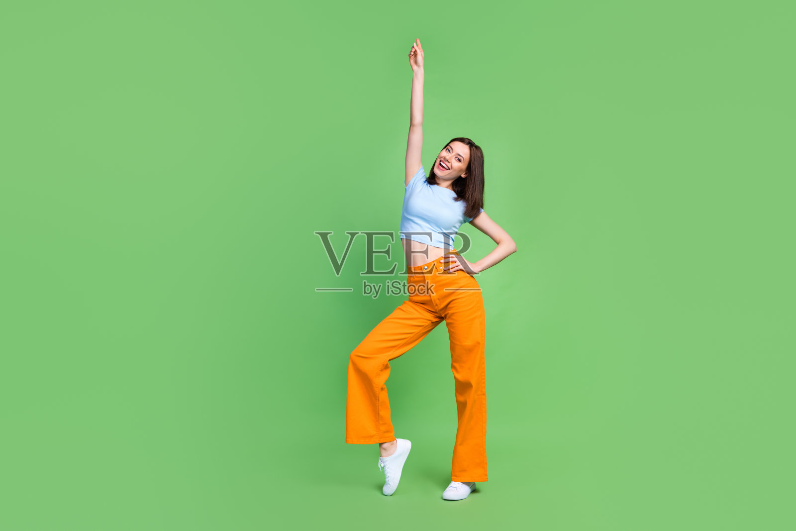 全身肖像，悠闲可爱的女士举起手臂，指着跳舞，背景为绿色。照片摄影图片