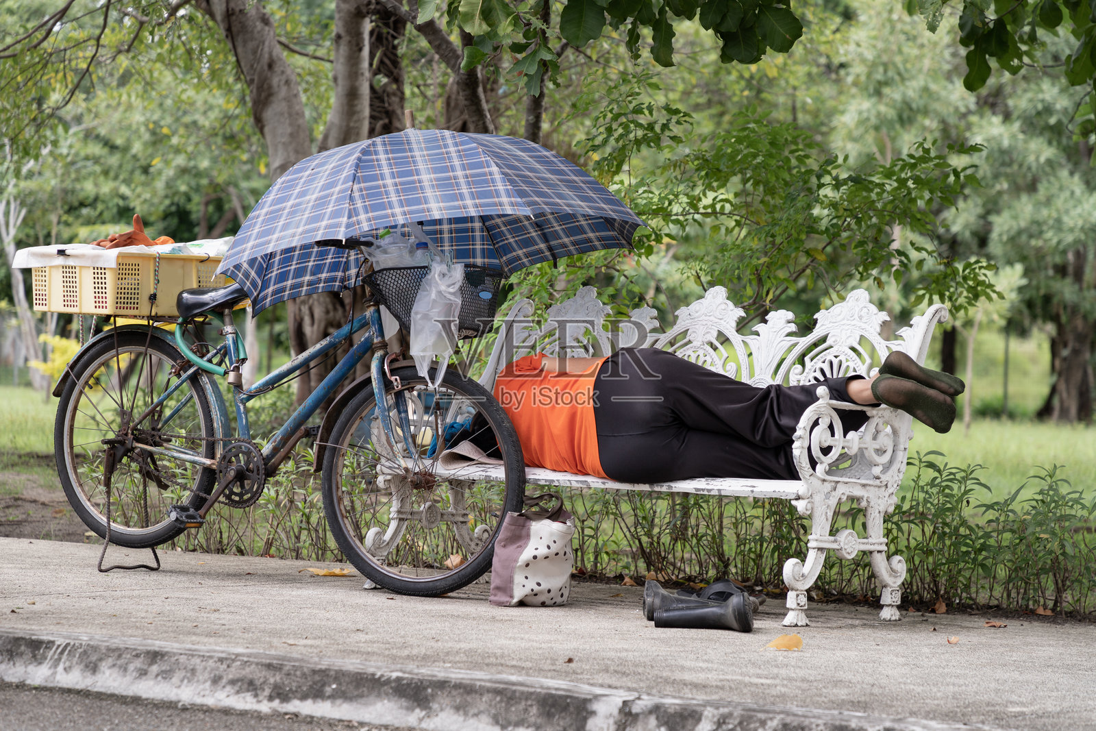 女人在公共长椅上睡觉时用手保护自己免受阳光照射。照片摄影图片