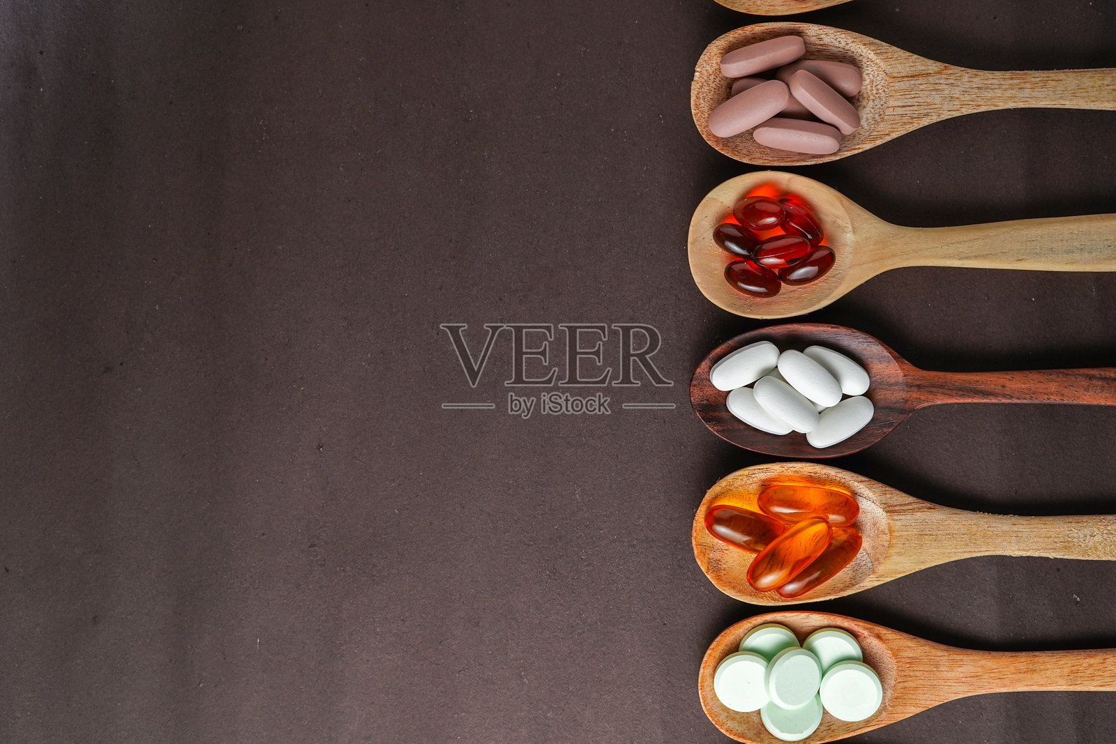 各种不同的药丸和维生素补充剂，放在黑色背景上的木勺里照片摄影图片