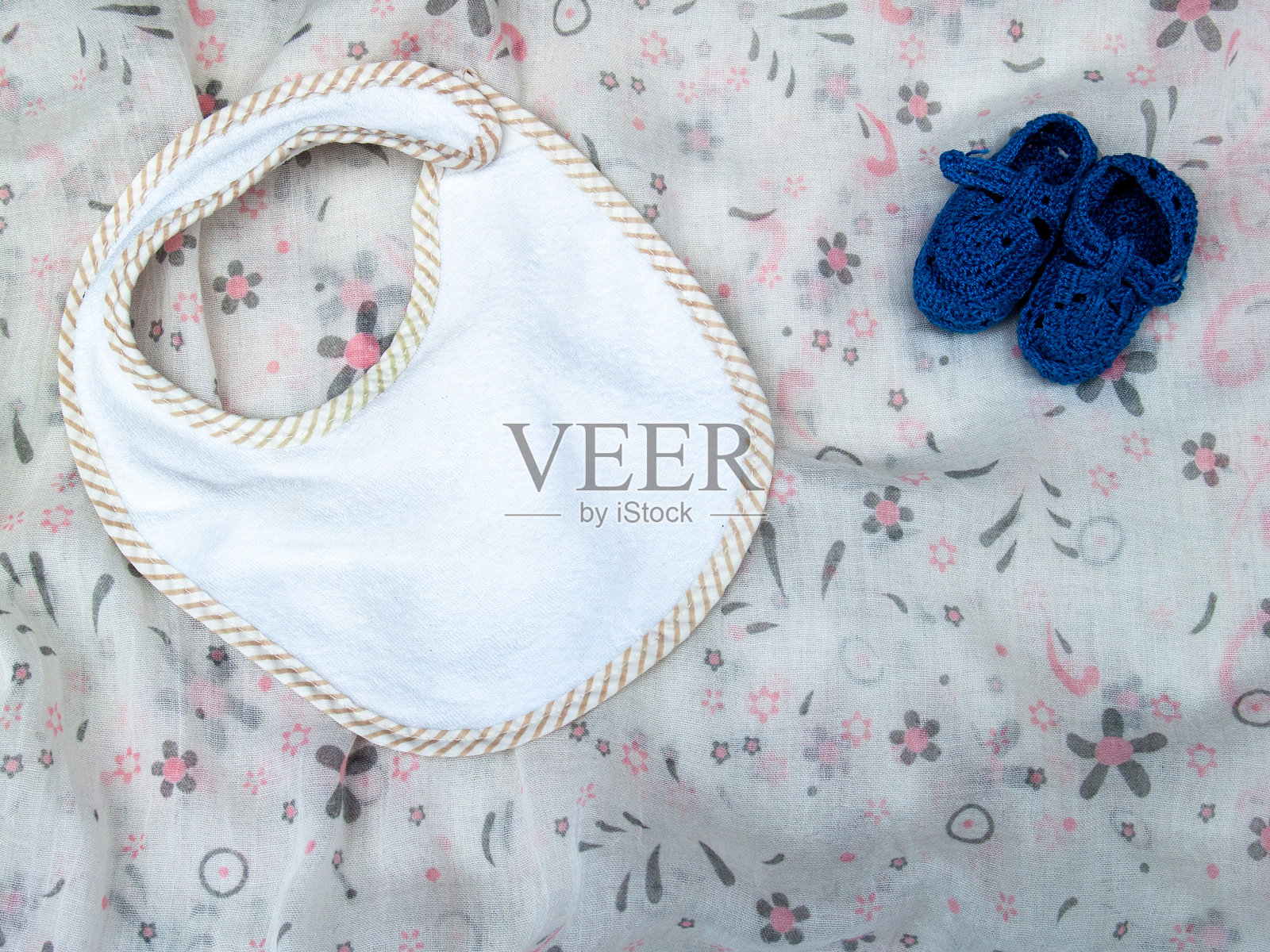 高角度视图的婴儿围嘴和小鞋子放在布料上照片摄影图片