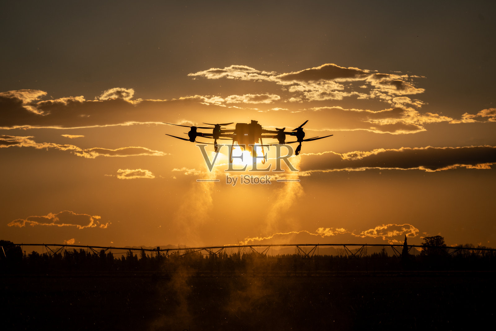 农业无人机在田间作业。田地施药。喷洒农药以防治害虫。农业领域的创新。新技术。空中视角。日落。照片摄影图片