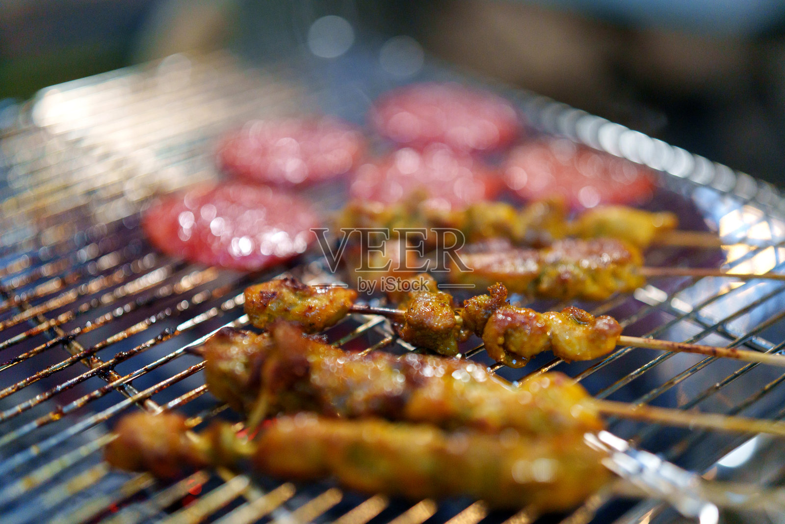 露营地的热闹场景中，烧烤架上摆放着滋滋作响的肉类和烤串，正炙烤在明火上。照片摄影图片