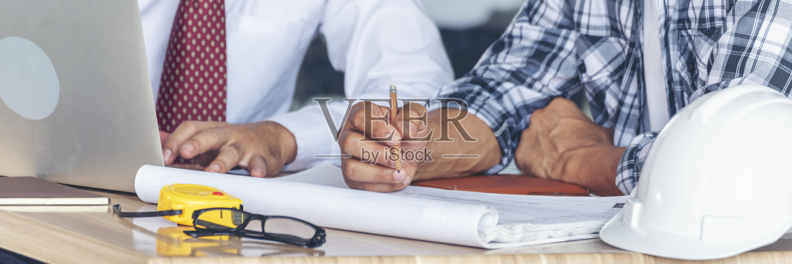 横幅承包商在建筑工地的建筑师桌子上与工程师会议。商人工程师经理与工头团队建设者一起讨论，使用卷尺，留有空白空间。照片摄影图片