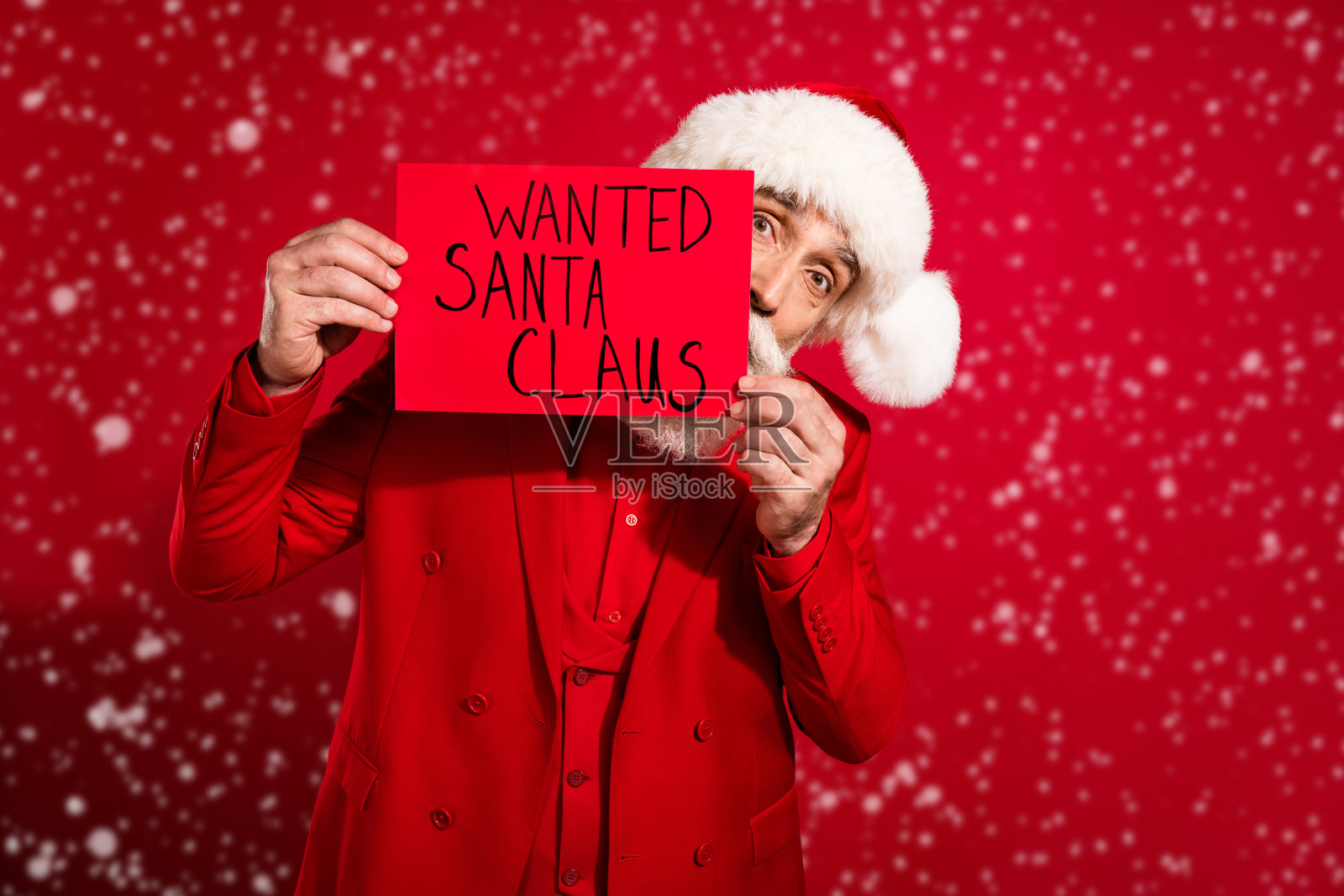 酷炫自信的快乐圣诞老人戴着太阳镜，穿着圣诞头饰和西装，背景为红色。照片摄影图片