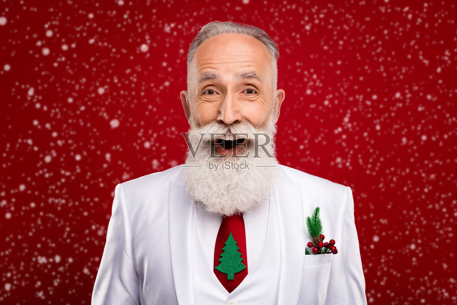 一位留着白色胡子的年长男性，穿着白色夹克，站在红色背景前，表情显得很惊讶。照片摄影图片