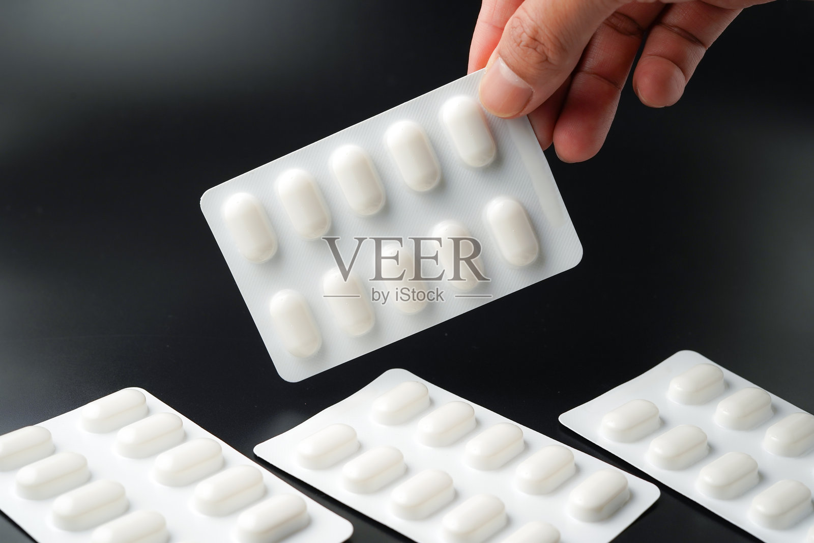 手握药片，药物胶囊在黑色背景下的泡罩包装中照片摄影图片