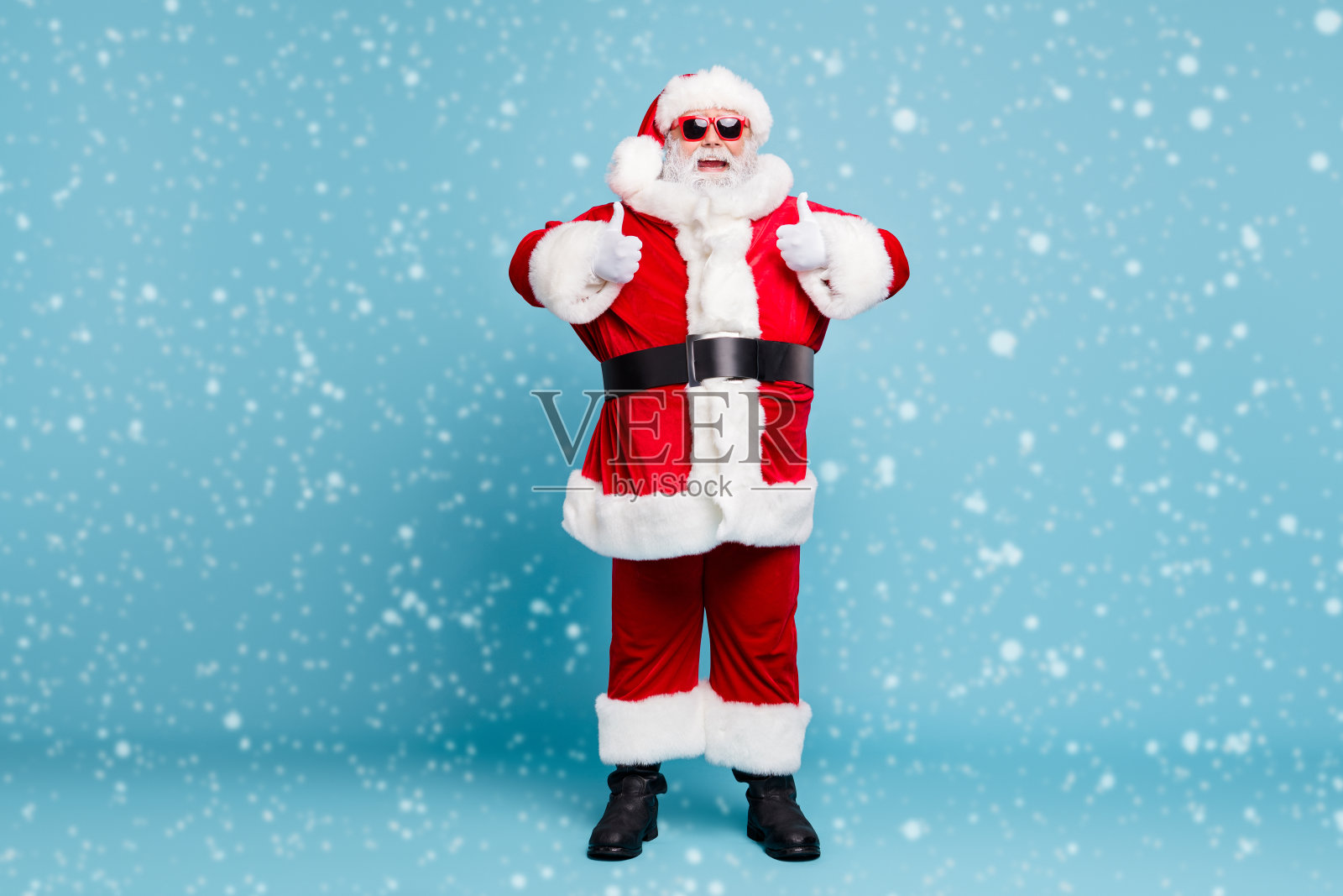 全身照，快乐、帅气、开心的胖胡子圣诞老人穿着温暖的冬季外套，双手竖起大拇指，背景为蓝绿色的柔和色调。照片摄影图片