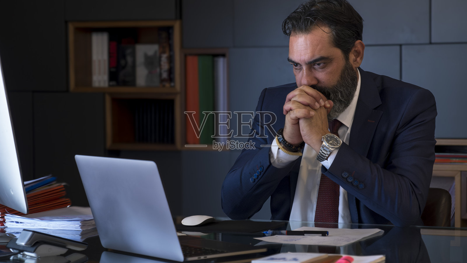 一位中年黑发商人在办公室的桌子上认真工作，专注于他的电脑。照片摄影图片