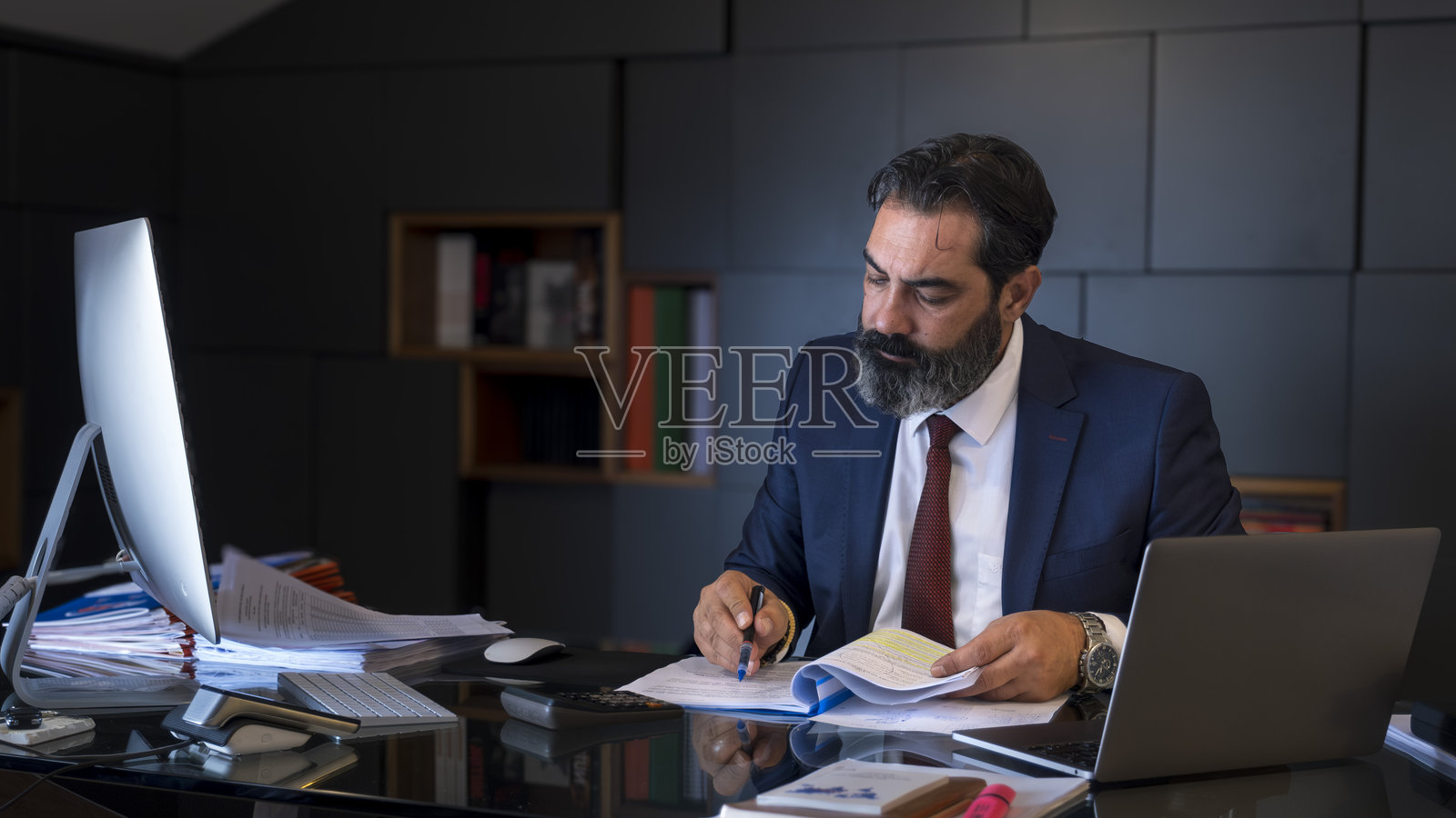 一位中年黑发商人在办公室的桌子上认真工作，专注于他的电脑。照片摄影图片