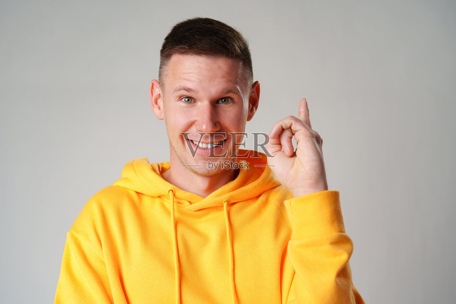 年轻的微笑男子穿着休闲服装，指向灰色墙壁上的上方照片摄影图片