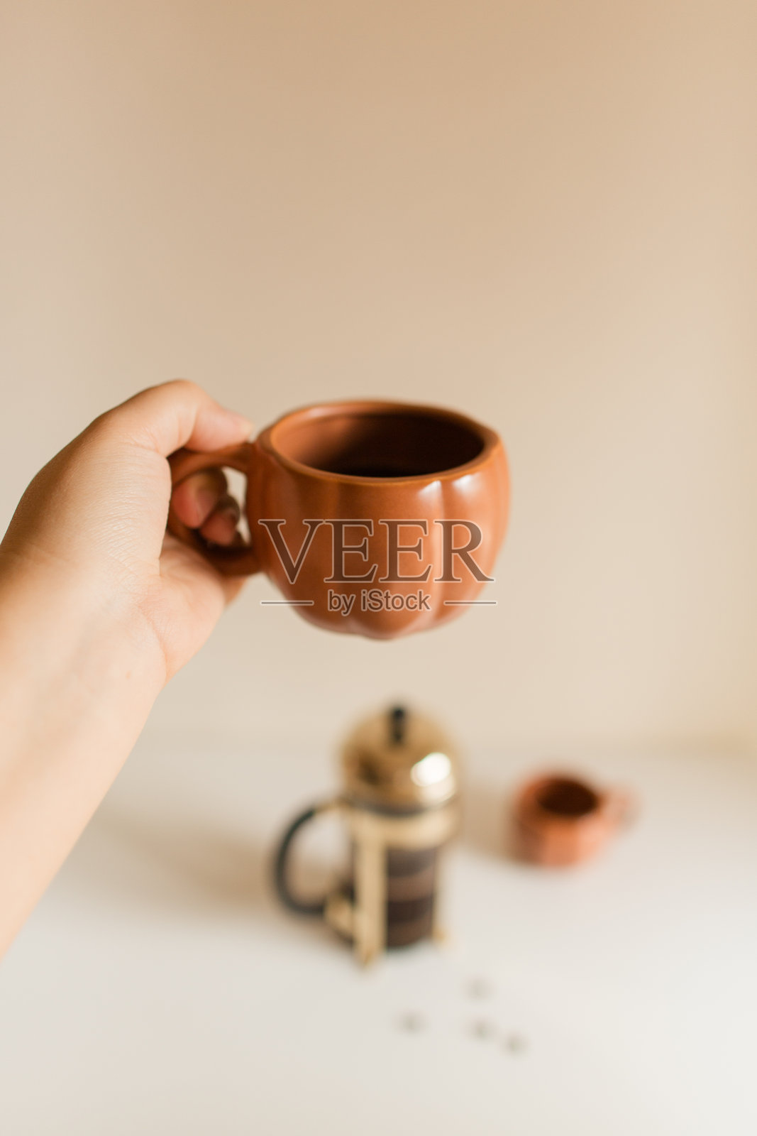 女人的手握着一个装有新鲜冲泡黑咖啡的南瓜杯，旁边是一台金色和黑色的玻璃法式压滤壶，背景是一个秋天的日子。照片摄影图片