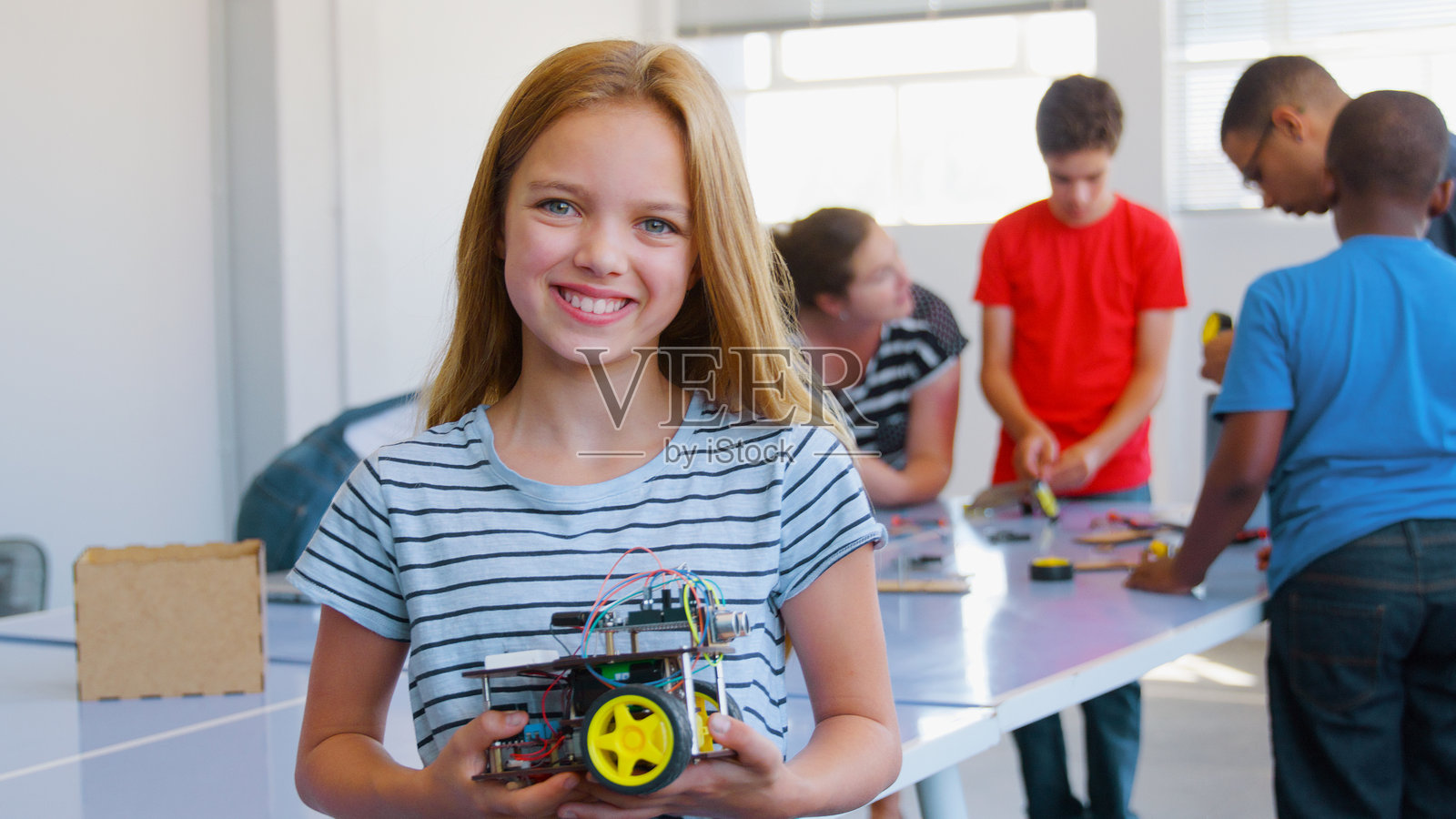 微笑的女学生在学校的计算机编程课上手持机器人车辆的肖像照片摄影图片