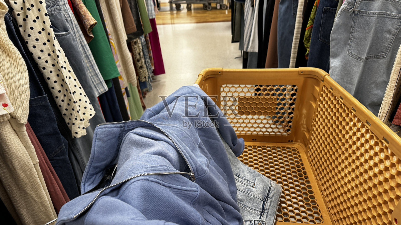 一个服装店的场景，前景中有一个黄色购物车，里面装着一件折叠的蓝色夹克和一条牛仔裤。照片摄影图片