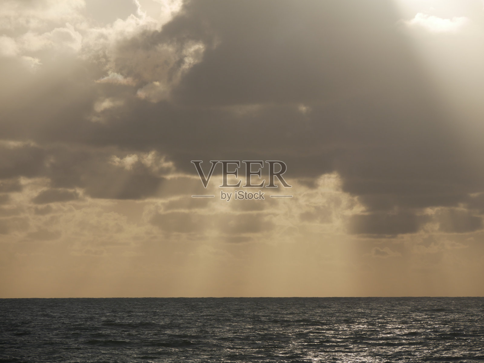 阳光透过云层洒在海洋上，夕阳的光辉照片摄影图片