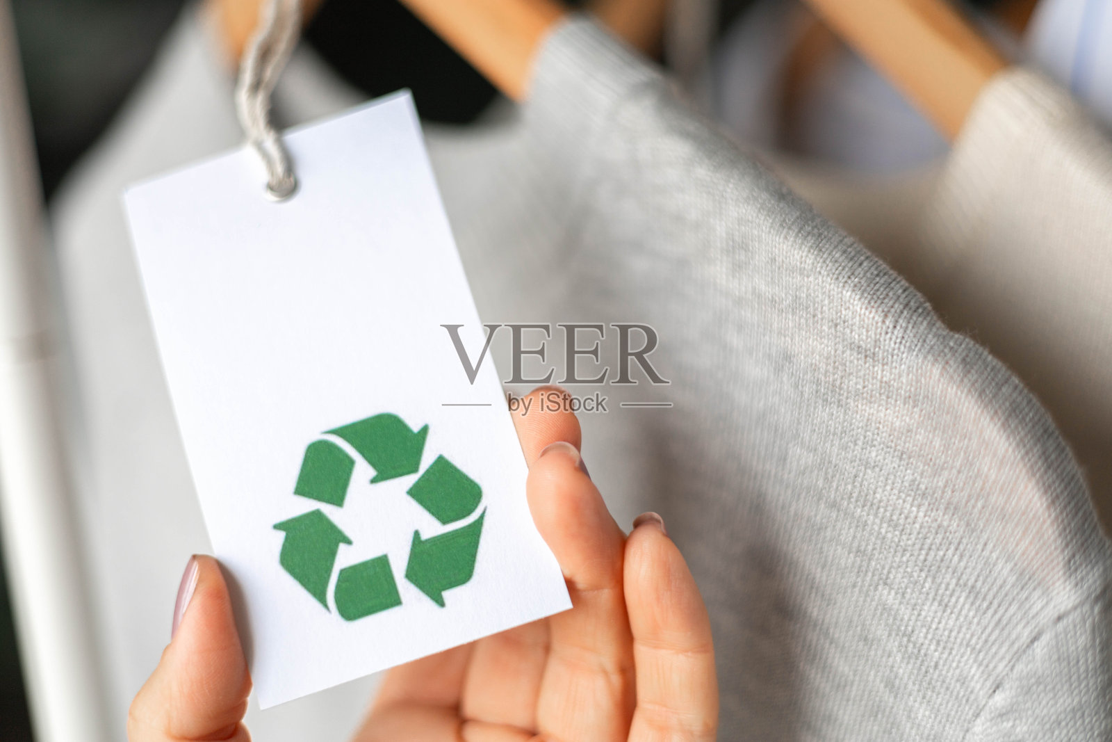 女性手握着一件白色针织衣物上的标签，上面描绘着回收标志。照片摄影图片