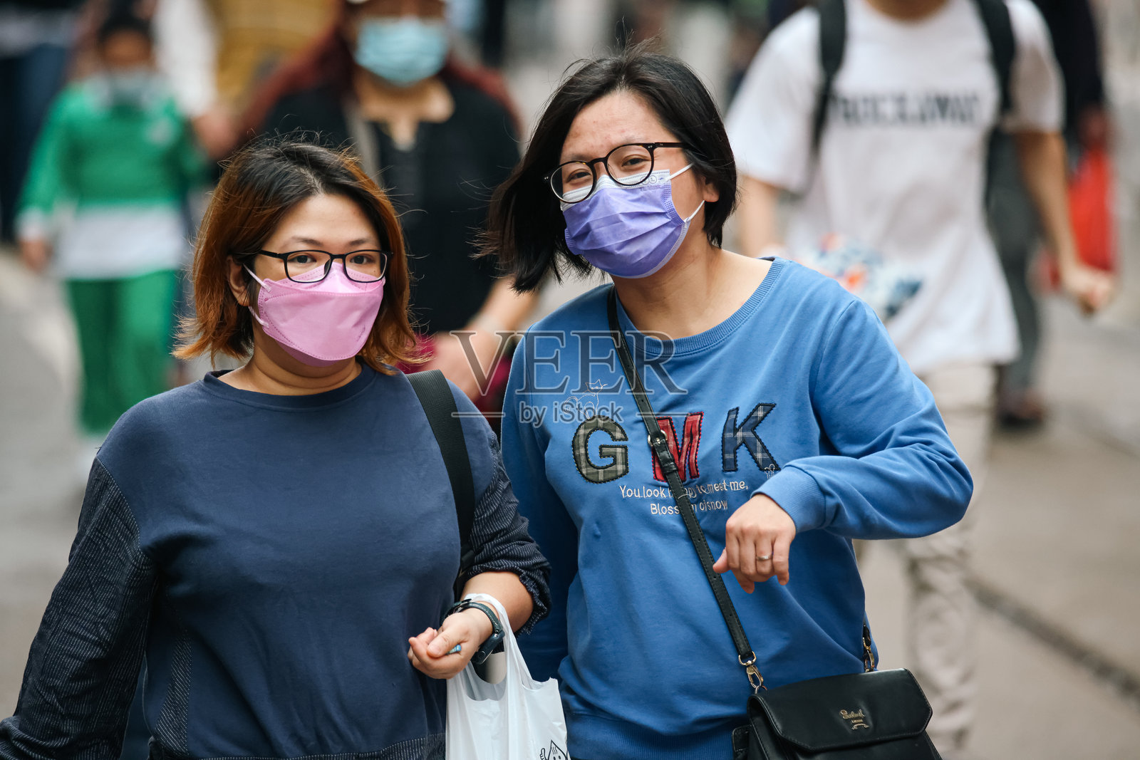 在繁忙的一天里，两名戴着口罩的妇女一起走在香港街头照片摄影图片