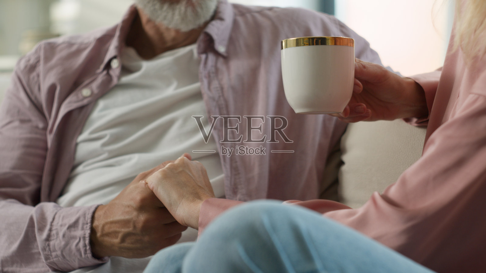 深爱、关心、温柔的白人老年男性丈夫亲吻心爱的妻子的手，妻子正在享用香浓的咖啡，享受温馨浪漫的爱情时刻，幸福的已婚老年夫妇在家中亲密相处。照片摄影图片