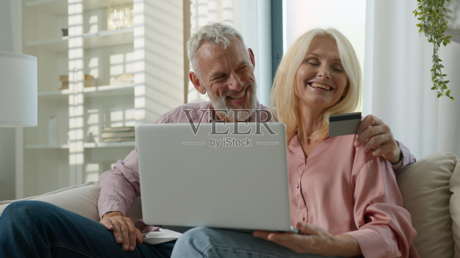 快乐的老年夫妇在家中一起使用笔记本电脑进行在线购物，互相拥抱，讨论购买事宜，安全地通过信用卡进行即时支付，享受电子银行服务。照片摄影图片