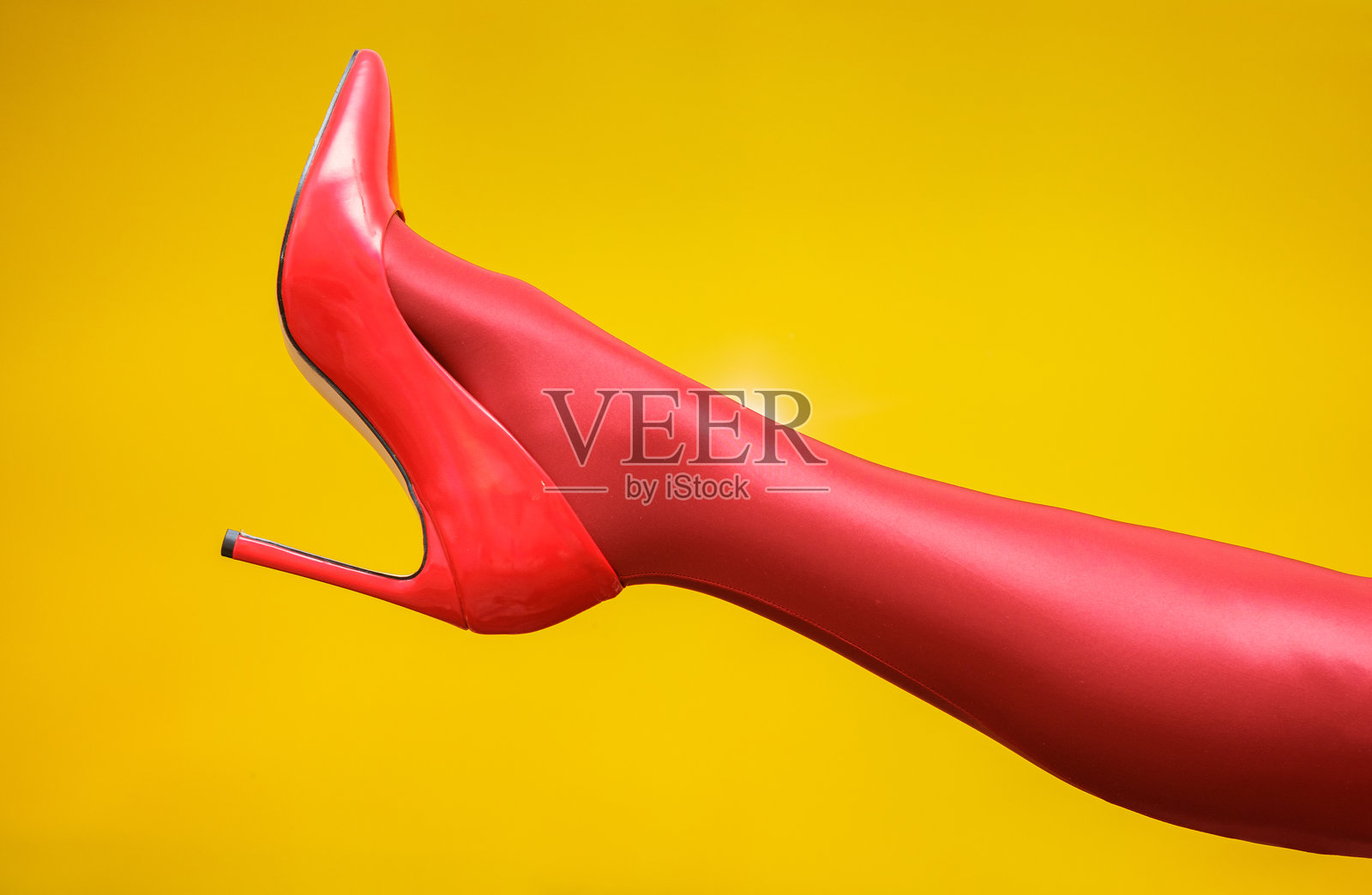 女性穿着红色紧身裤和细高跟鞋的腿，背景为黄色。照片摄影图片