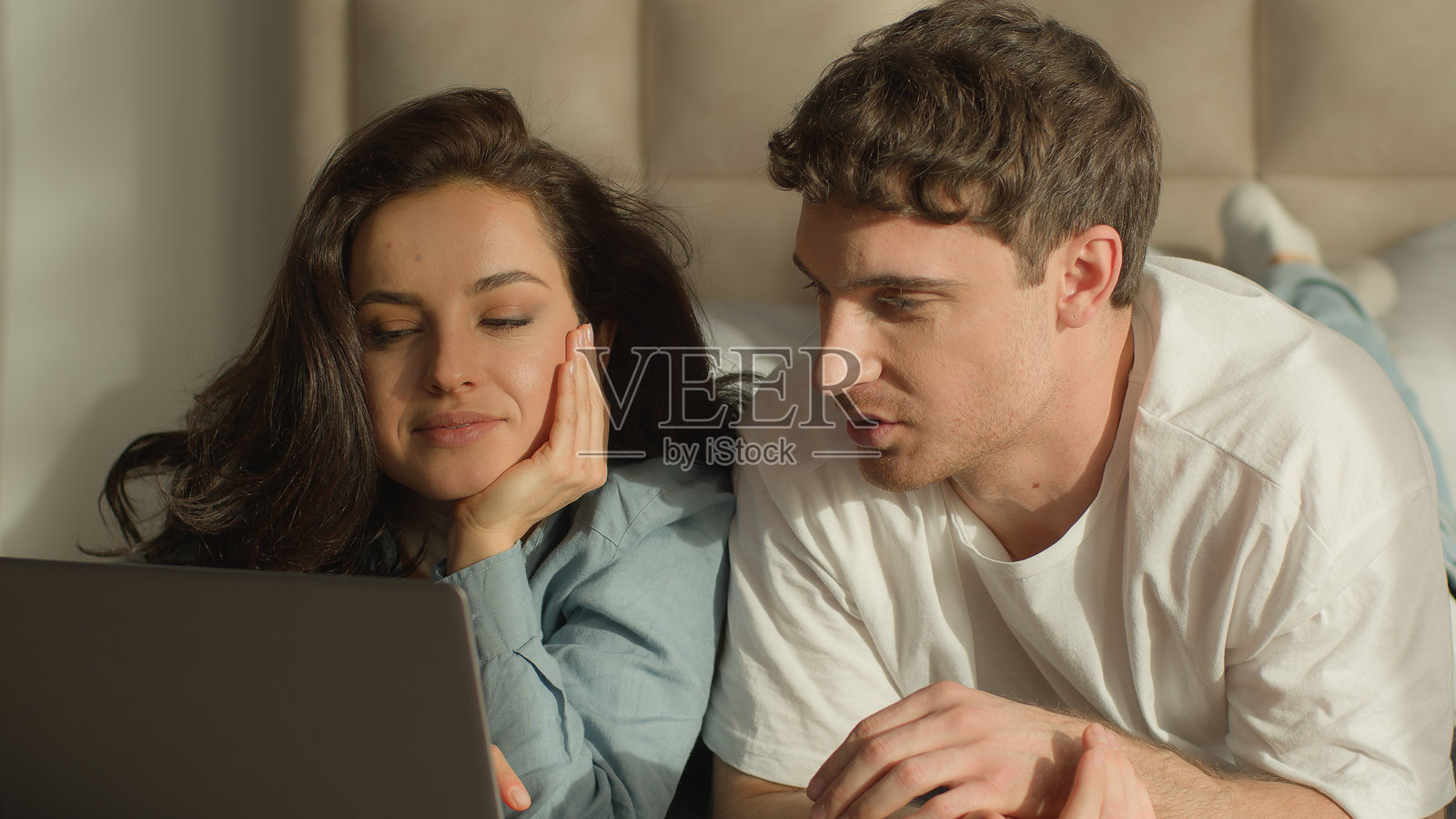 男女情侣在卧室的床上用笔记本电脑观看电影，享受周末的约会时光，聊天讨论。照片摄影图片