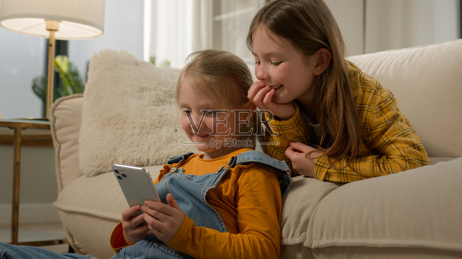 两个快乐的白人女孩姐妹在客厅沙发上一起玩手机，享受在线游戏和浏览社交网络的乐趣。照片摄影图片