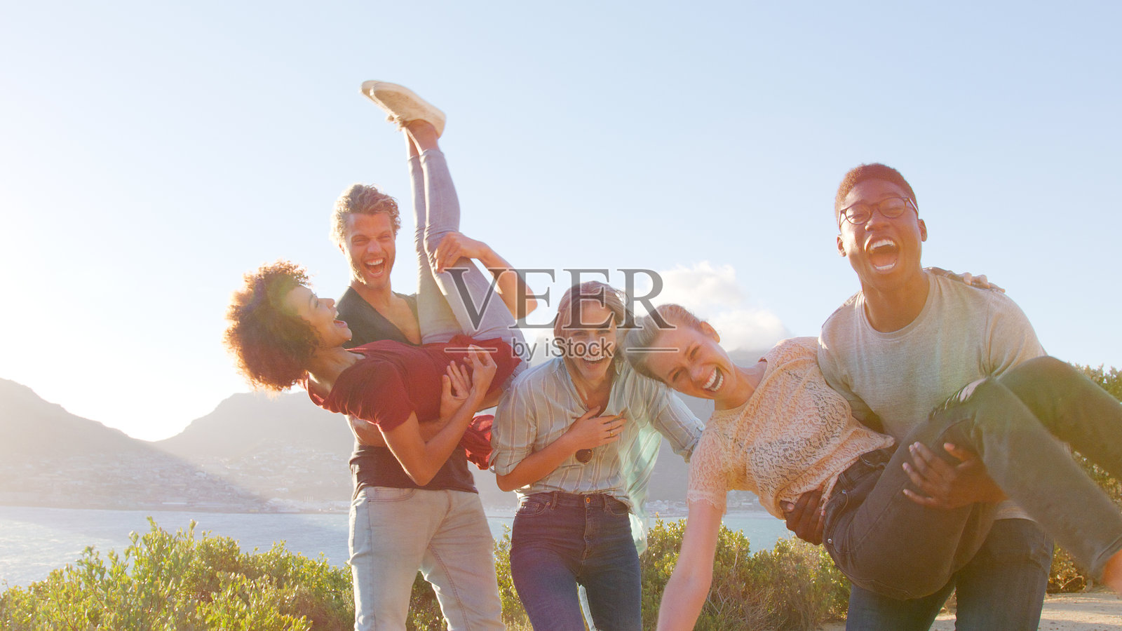 情侣们玩得开心，男人们把女人举起来，一群朋友在海岸小道上散步。照片摄影图片