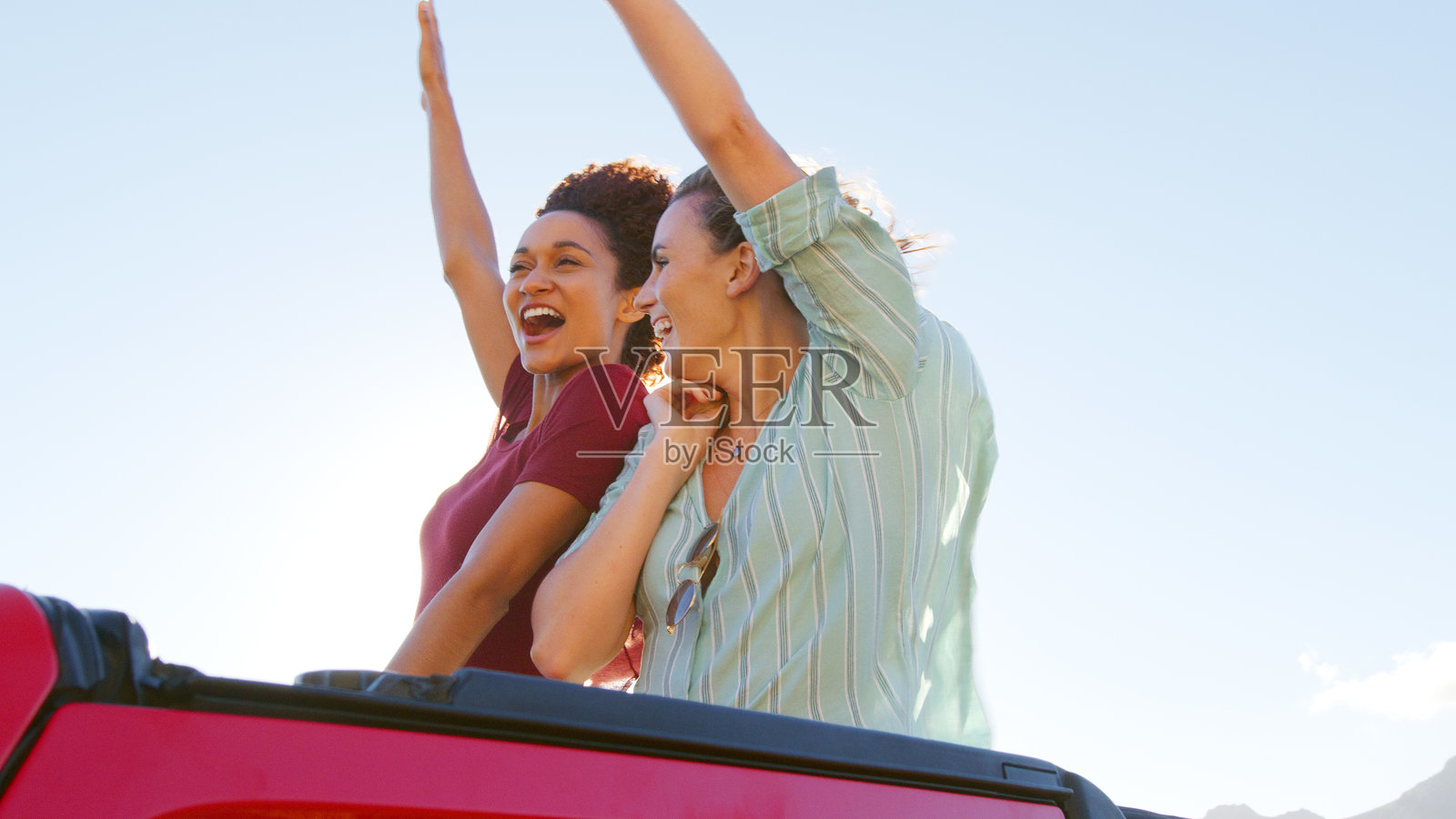 两个女性朋友在夏季假期中站在敞篷租车的后面照片摄影图片
