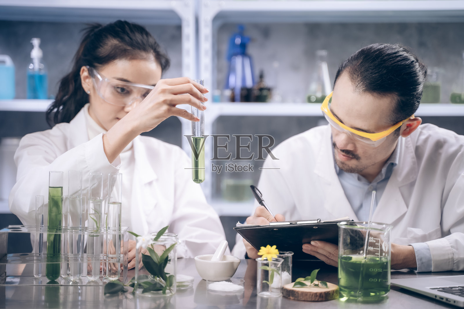 两位研究人员在化妆品实验室里手持试管，正在讨论和记录关于物质的内容。他们对自己的研究感到开心。照片摄影图片