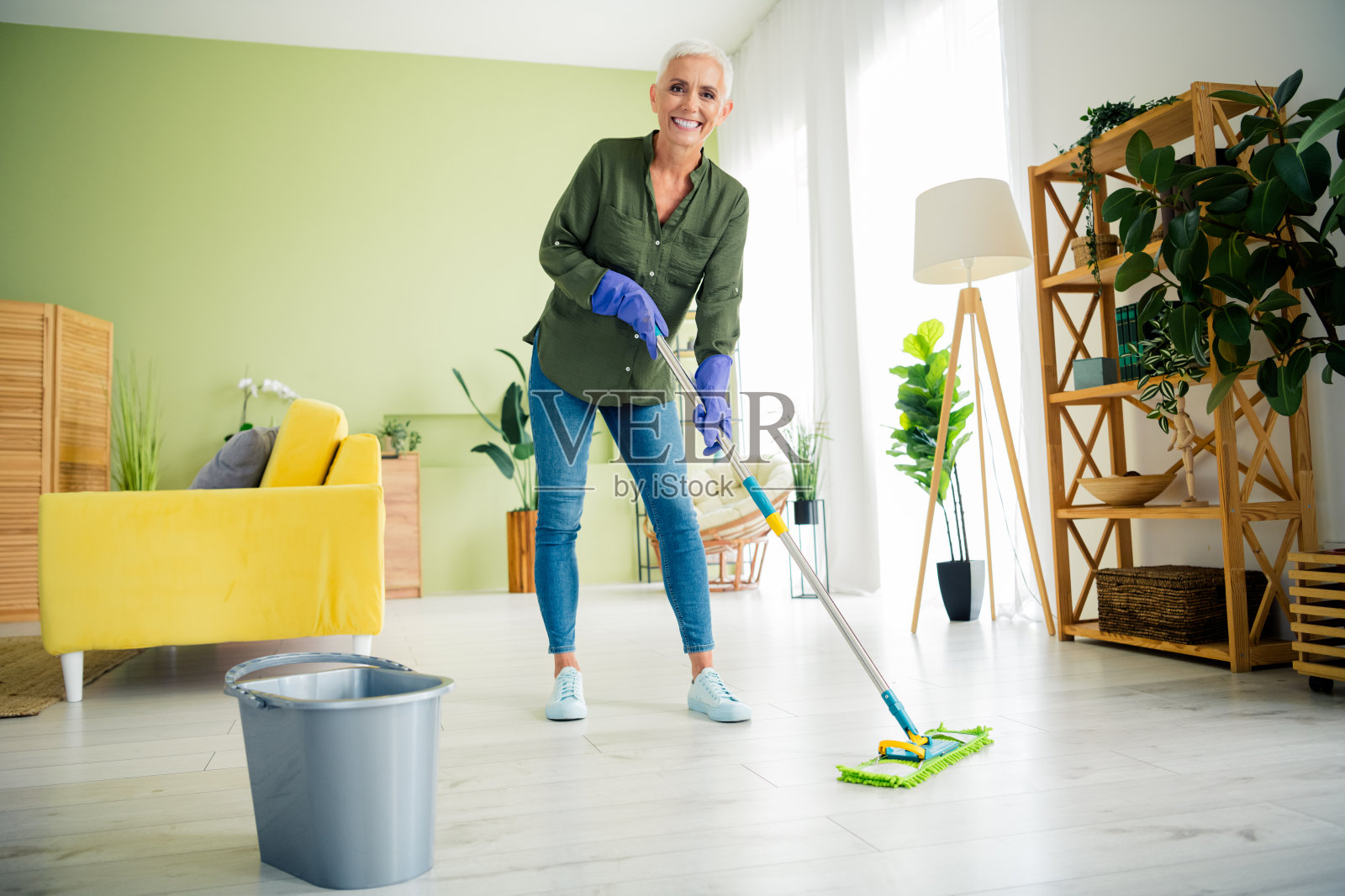 穿着绿色衬衫的漂亮快乐女士在室内家中微笑着清洗地板照片摄影图片