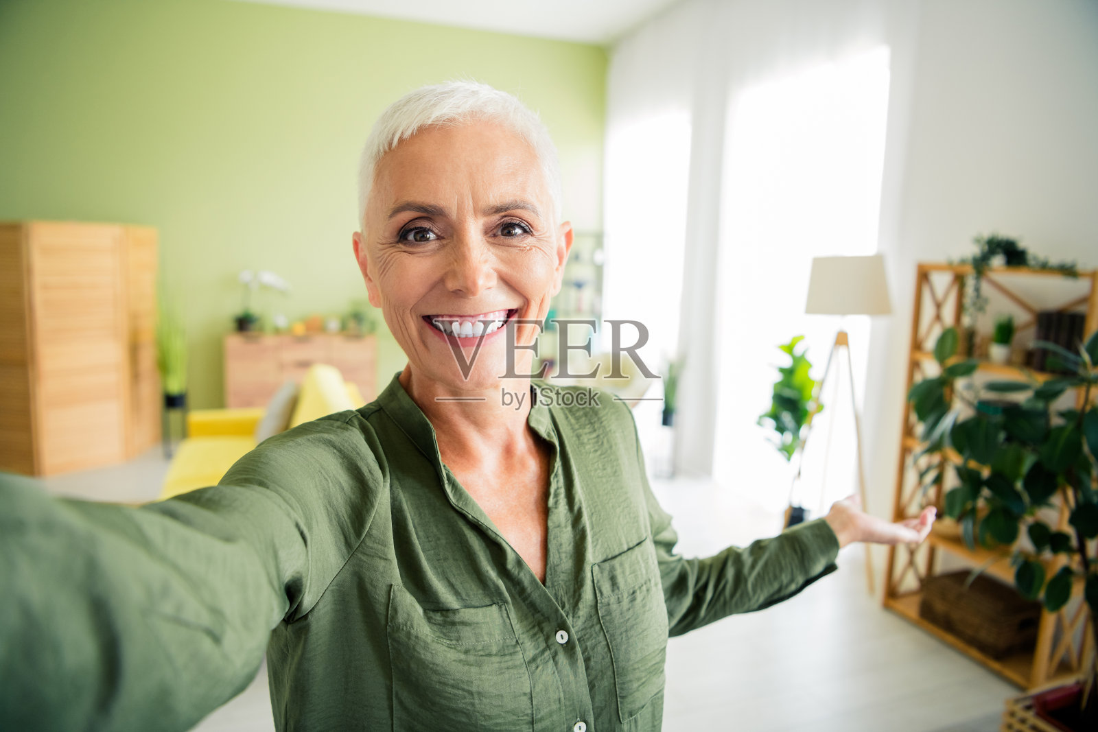 漂亮快乐的女士穿着绿色衬衫，在室内公寓录制视频博客。照片摄影图片